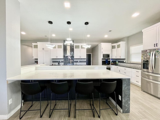 kitchen featuring a breakfast bar, stainless steel appliances, decorative backsplash, white cabinets, and decorative light fixtures