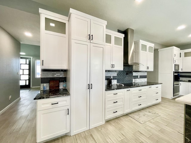 kitchen featuring white cabinetry, light hardwood / wood-style floors, dark stone counters, and wall chimney exhaust hood