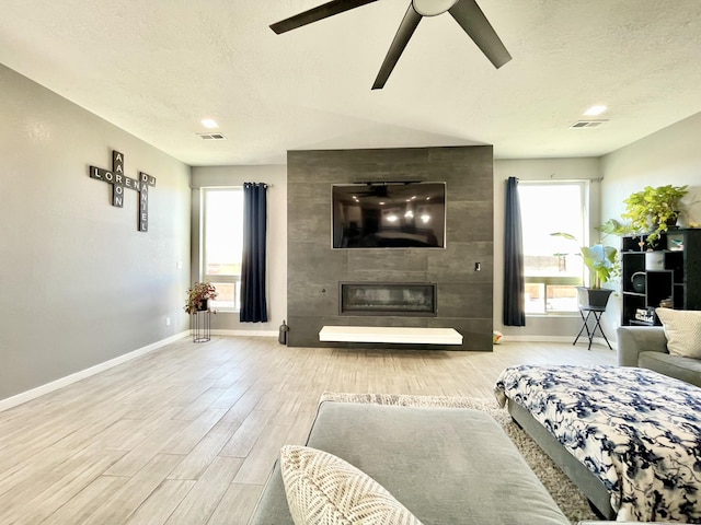 living room with ceiling fan, a fireplace, and a textured ceiling