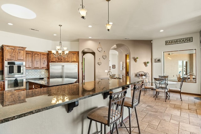 kitchen with a breakfast bar, sink, hanging light fixtures, stainless steel appliances, and backsplash