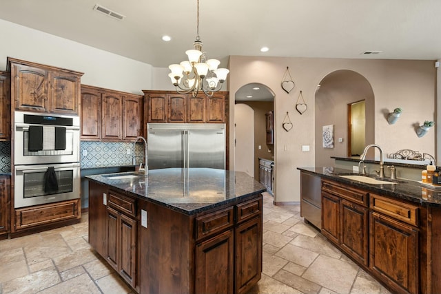 kitchen featuring a kitchen island with sink, sink, dark stone countertops, and appliances with stainless steel finishes