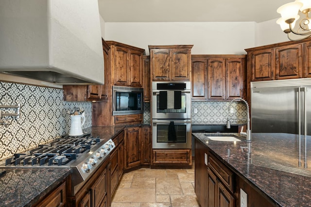 kitchen featuring premium range hood, dark stone counters, built in appliances, and backsplash