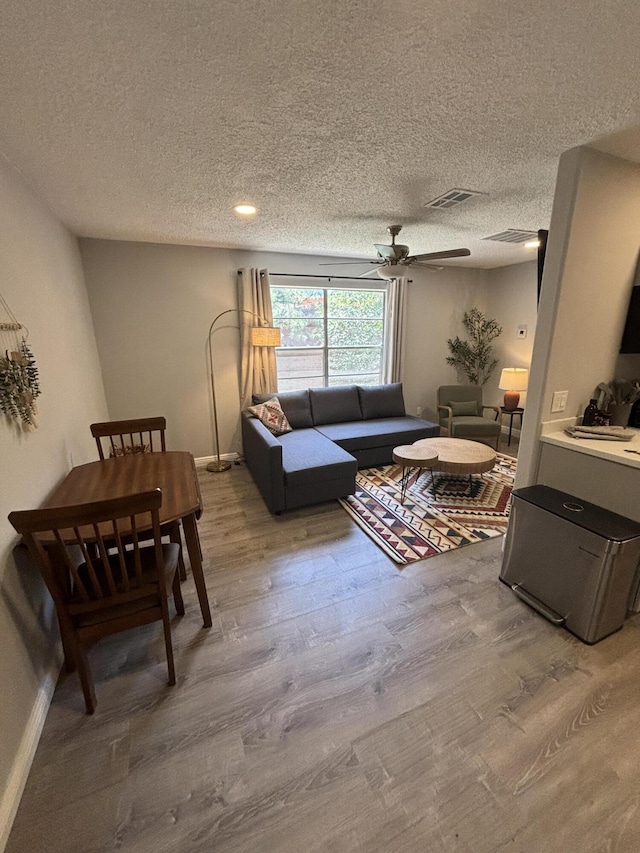 living room with hardwood / wood-style flooring, ceiling fan, and a textured ceiling