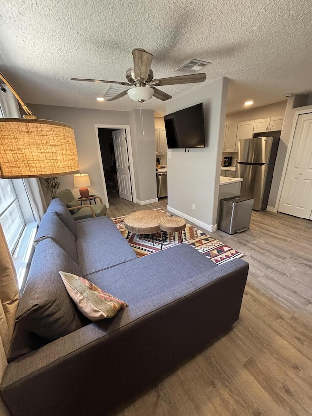 living room featuring a textured ceiling, ceiling fan, and light wood-type flooring