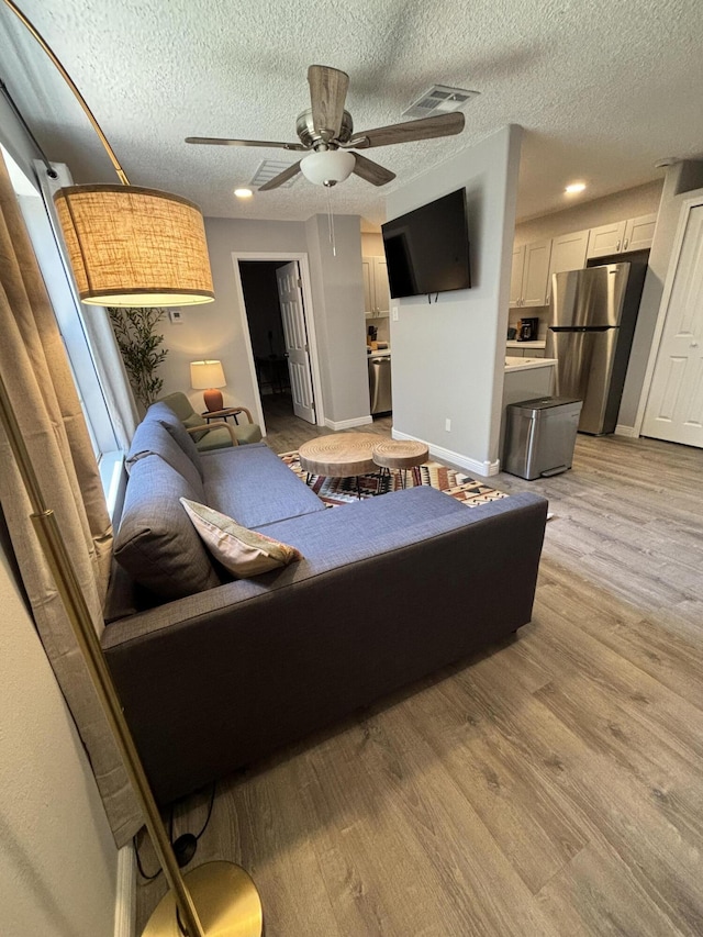 living room featuring ceiling fan, a textured ceiling, and light hardwood / wood-style floors