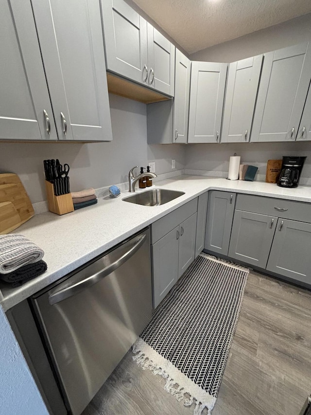 kitchen featuring sink, light hardwood / wood-style flooring, dishwasher, gray cabinetry, and a textured ceiling