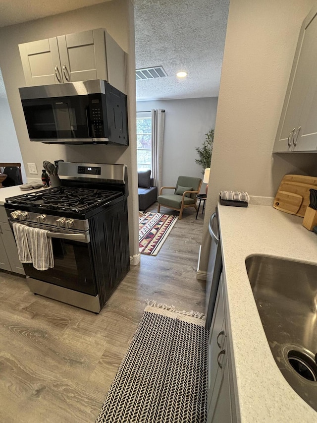 kitchen featuring stainless steel gas range oven, sink, a textured ceiling, and light hardwood / wood-style floors