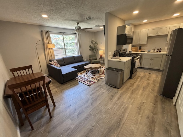 living room featuring sink, light hardwood / wood-style floors, a textured ceiling, and ceiling fan