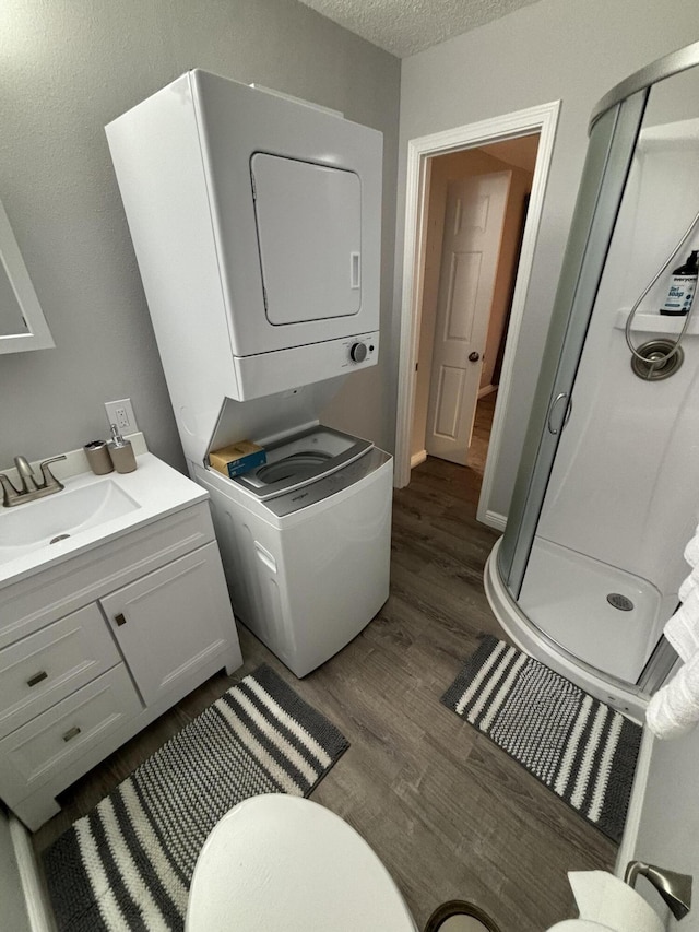 clothes washing area featuring sink, dark hardwood / wood-style floors, a textured ceiling, and stacked washing maching and dryer