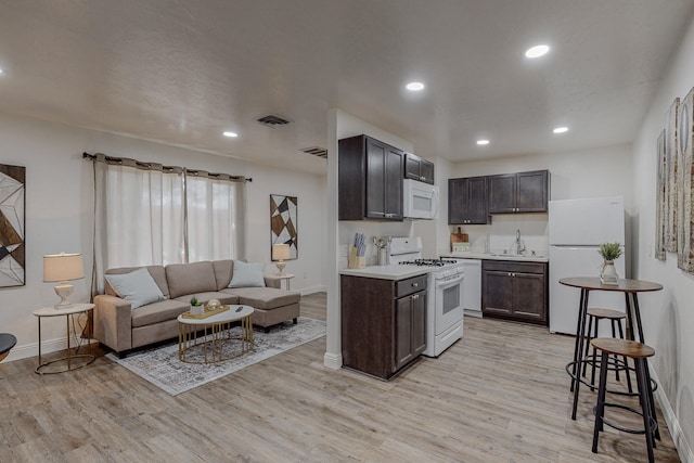 kitchen with dark brown cabinetry, light wood-type flooring, sink, and white appliances