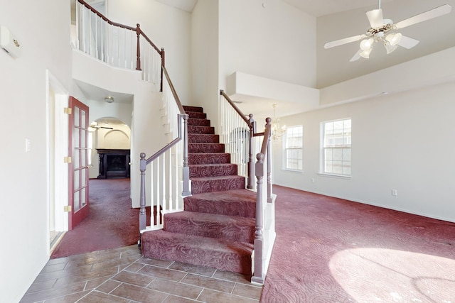 stairway featuring ceiling fan with notable chandelier, carpet floors, and a high ceiling