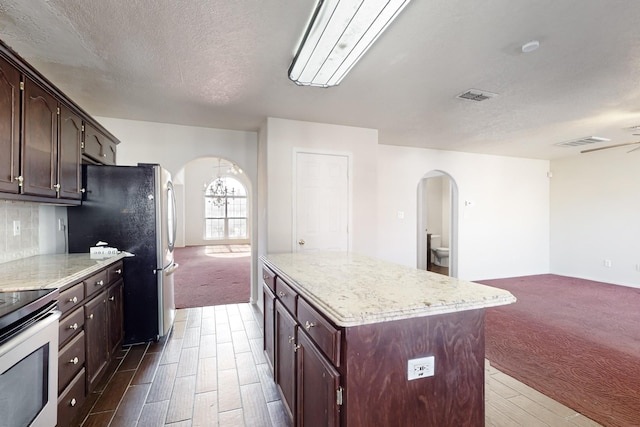 kitchen featuring appliances with stainless steel finishes, a center island, dark colored carpet, dark brown cabinetry, and decorative backsplash