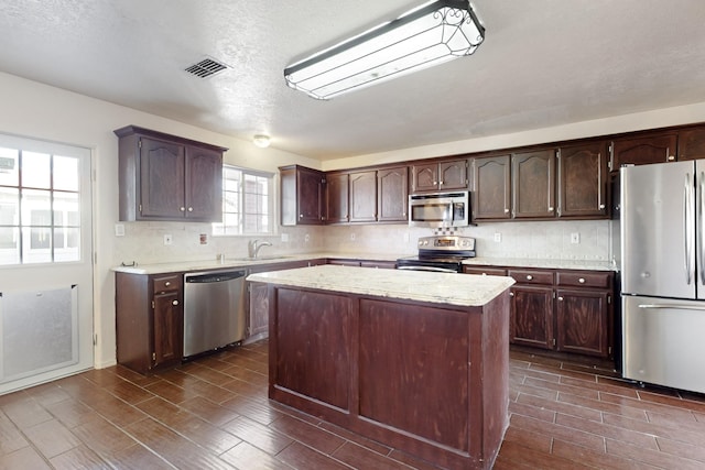 kitchen featuring a kitchen island, appliances with stainless steel finishes, dark brown cabinets, and decorative backsplash