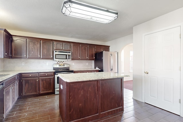 kitchen featuring backsplash, a center island, stainless steel appliances, light stone countertops, and dark brown cabinets