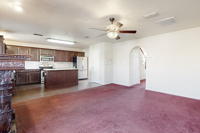 kitchen featuring ceiling fan, dark brown cabinets, stainless steel appliances, a center island, and dark carpet