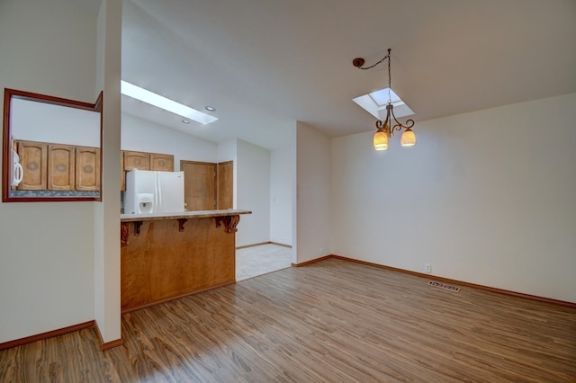 unfurnished living room featuring vaulted ceiling with skylight, a chandelier, and light hardwood / wood-style flooring