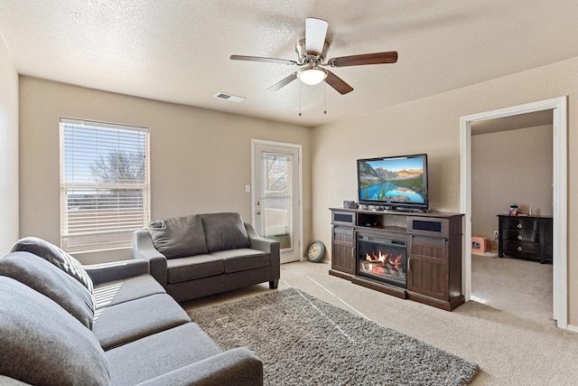 carpeted living room with ceiling fan, plenty of natural light, and a textured ceiling