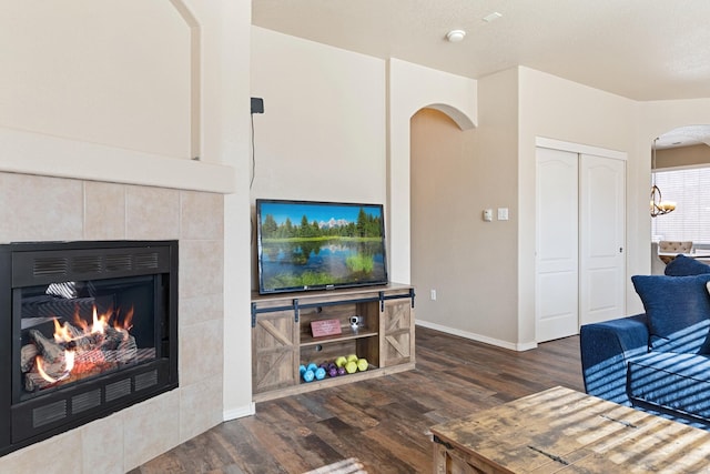 living room featuring a tiled fireplace and dark wood-type flooring