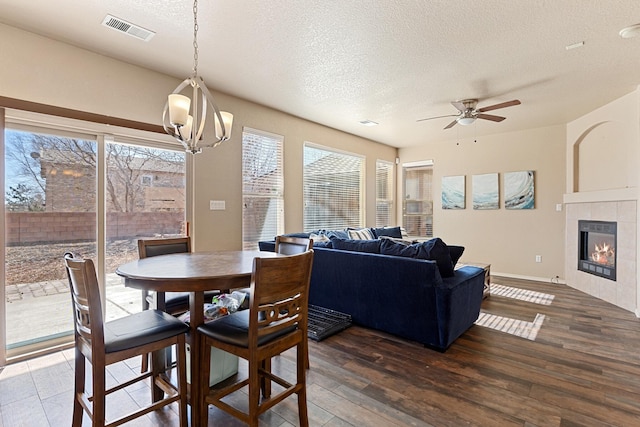 dining room featuring a tiled fireplace, ceiling fan with notable chandelier, a textured ceiling, and dark hardwood / wood-style flooring