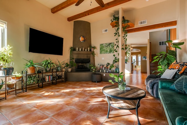 living room with tile patterned floors, a large fireplace, beamed ceiling, ceiling fan, and a high ceiling