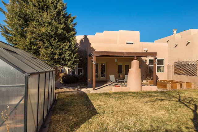 rear view of property with french doors, an outdoor structure, a patio area, and a lawn