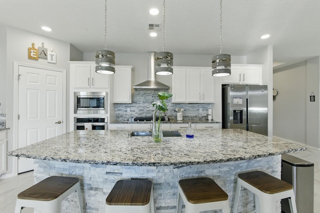 kitchen with visible vents, wall chimney range hood, a breakfast bar, stainless steel appliances, and a sink