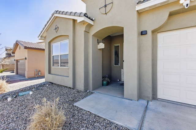 entrance to property with a tile roof, a garage, and stucco siding