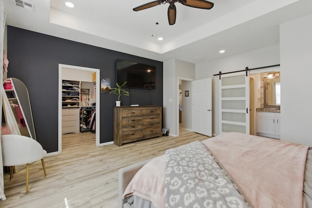 bedroom featuring a walk in closet, a tray ceiling, a barn door, recessed lighting, and wood finished floors