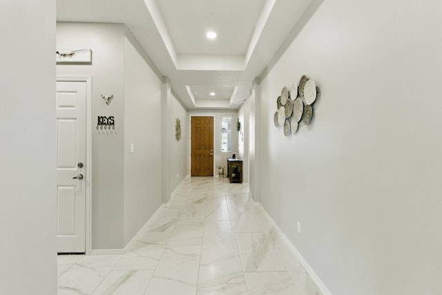 corridor with recessed lighting, baseboards, a raised ceiling, and marble finish floor