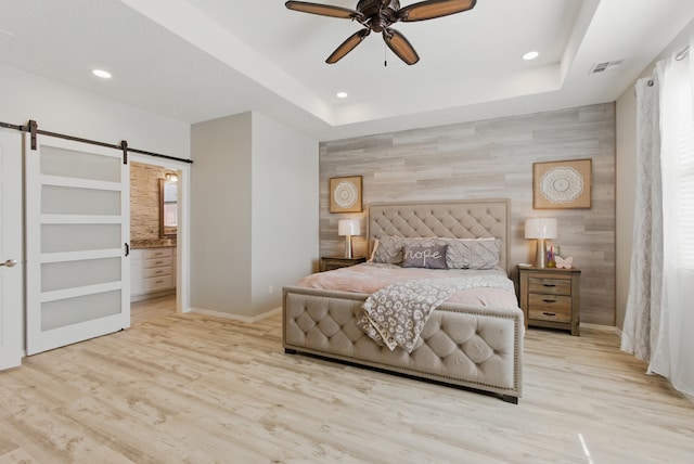 bedroom featuring an accent wall, a barn door, visible vents, and a raised ceiling