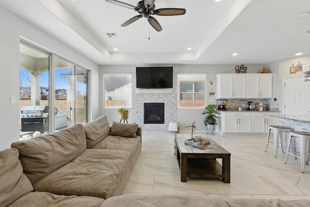 living area featuring visible vents, recessed lighting, a glass covered fireplace, a raised ceiling, and marble finish floor