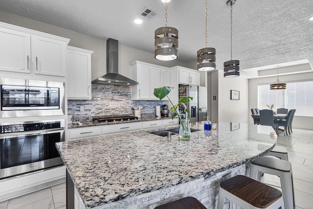 kitchen featuring appliances with stainless steel finishes, a breakfast bar area, pendant lighting, and wall chimney exhaust hood