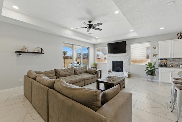 living room with a glass covered fireplace, a raised ceiling, plenty of natural light, and baseboards