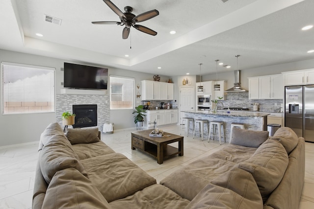 living room featuring a glass covered fireplace, a tray ceiling, baseboards, and visible vents