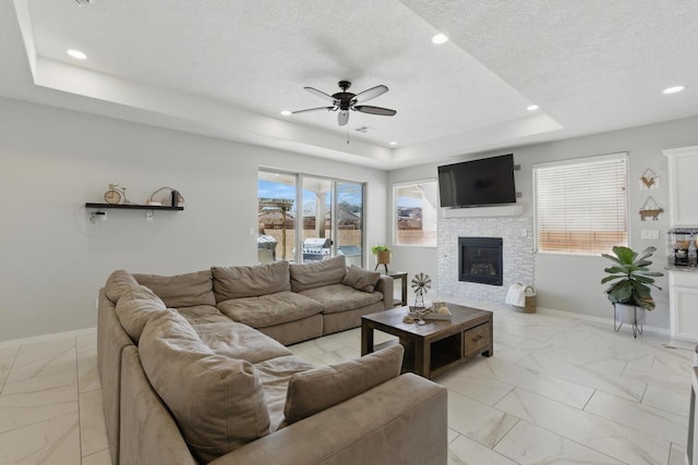 living room with baseboards, a tray ceiling, recessed lighting, a textured ceiling, and a glass covered fireplace