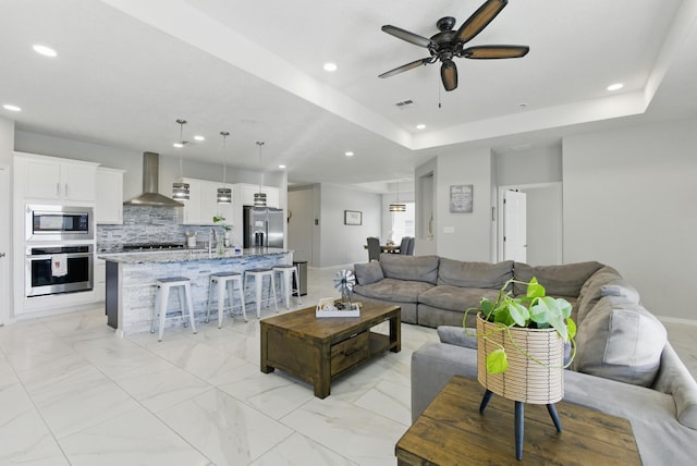 living area with recessed lighting, marble finish floor, visible vents, and a tray ceiling