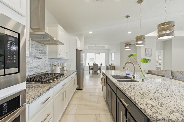 kitchen with a spacious island, a sink, stainless steel appliances, white cabinets, and wall chimney exhaust hood