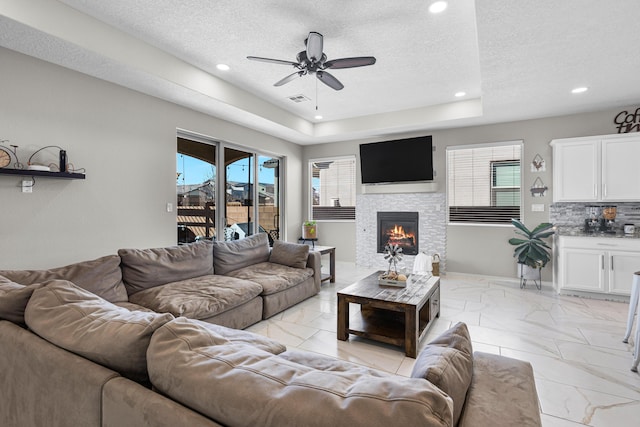 living room with ceiling fan, a stone fireplace, and a textured ceiling