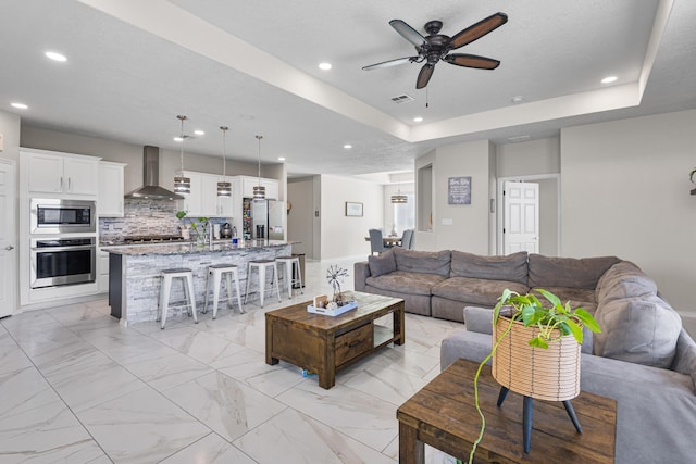 living room with a tray ceiling, a textured ceiling, and ceiling fan