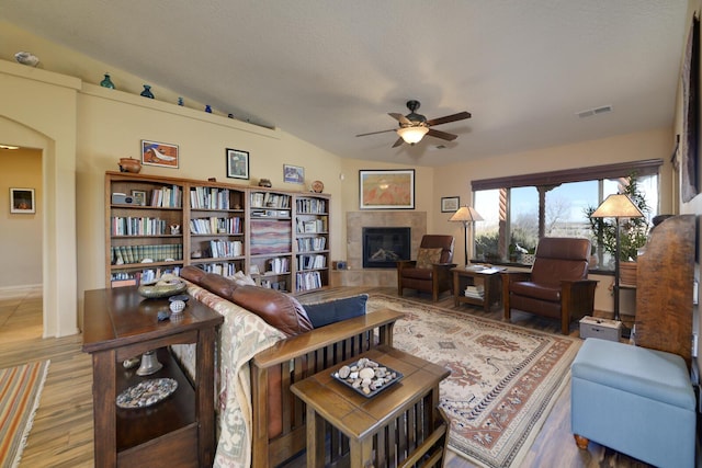 living room with a tiled fireplace, wood-type flooring, vaulted ceiling, and ceiling fan