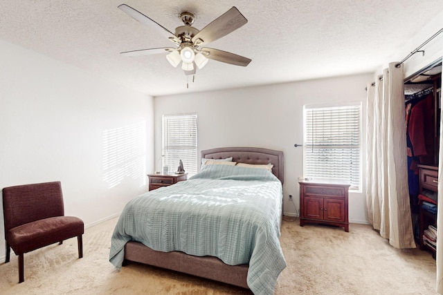 bedroom with ceiling fan, light carpet, and a textured ceiling