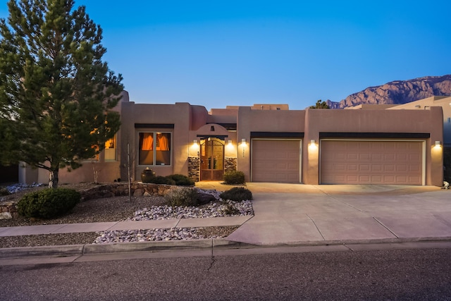 adobe home with an attached garage, driveway, and stucco siding