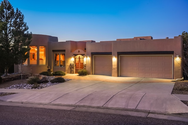 pueblo-style home featuring stucco siding, an attached garage, and driveway