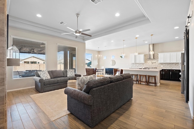 living room featuring a raised ceiling, ceiling fan with notable chandelier, and light hardwood / wood-style flooring