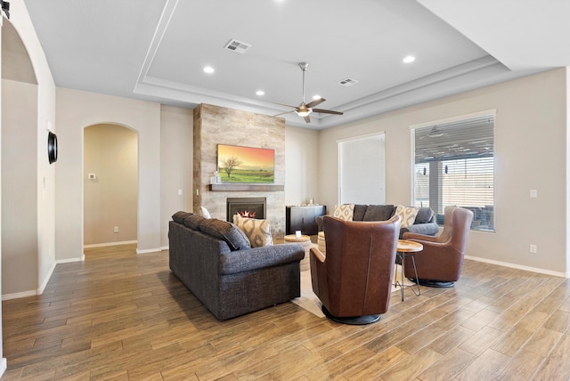 living room with hardwood / wood-style flooring, ceiling fan, a fireplace, and a raised ceiling