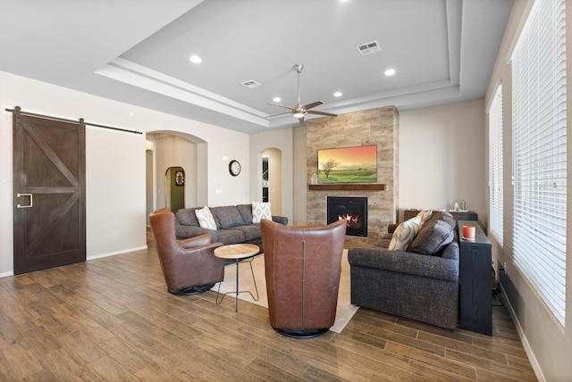 living room with hardwood / wood-style flooring, a large fireplace, a tray ceiling, and ceiling fan