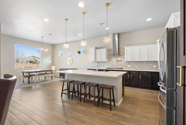 kitchen featuring pendant lighting, a breakfast bar area, wall chimney range hood, stainless steel appliances, and a center island with sink