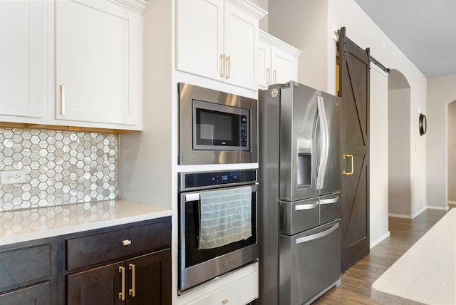 kitchen featuring stainless steel appliances, a barn door, hardwood / wood-style floors, decorative backsplash, and white cabinets