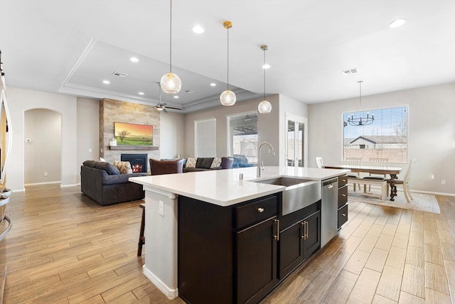 kitchen with sink, dishwasher, pendant lighting, a fireplace, and a kitchen island with sink