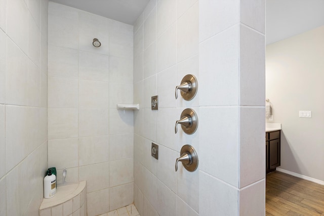 bathroom featuring hardwood / wood-style flooring, tiled shower, and vanity